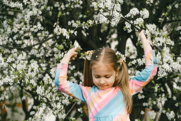 春の自然を探索する開花庭で素敵な小さな子供 木を揺らし花びらが頭の上に落ちてくる 庭の楽しみ — ストック写真