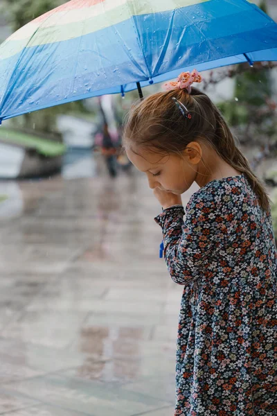 市内の雨の下を歩く傘を持つ子供 家の近くに虹色の傘を持つ幸せな女の子 水たまりと暖かい雨の夏の天気 — ストック写真