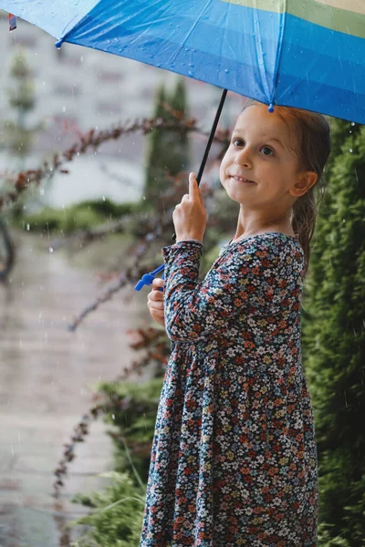 孩子们 带着雨伞在城市里走着 快乐的女孩 带着彩虹色的雨伞在房子附近 温暖潮湿的夏天 还有水坑 — 图库照片