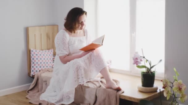 中年妇女每天早上都会在窗台上看一本书 浪漫舒适的家庭氛围 身体正面和自然女性美 — 图库视频影像