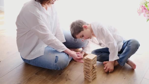 子供の息子と母の床の物理的なスキルタワーのボードゲームをプレイして座っている 塔を破壊した 日当たりの良い窓から Jenga 54木製のブロックのジャンガ 家庭で人気のファミリーゲーム — ストック動画