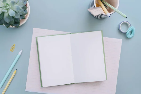 Pastel mavi arka planda ofis malzemeleri olan boş bir defter. Ofis yatıyordu. Boş kağıt. Yaratıcı iş, öğrenim ya da planlama için çalışma masası