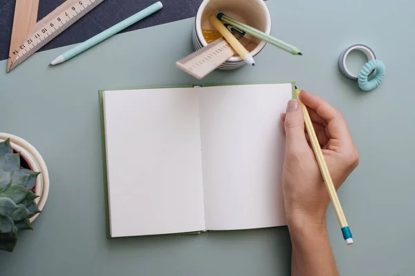 Kadınların elleri, pastel mavisi arka plandaki boş deftere yazmaya hazır. Mesaj için yer. Yaratıcı iş, öğrenim ya da planlama için çalışma masası