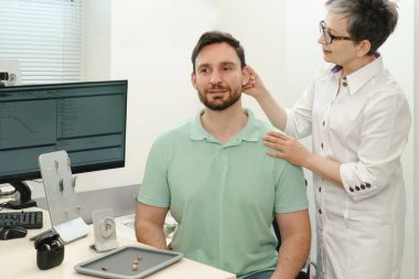 Adam klinikte modern kompakt işitme cihazı deniyor. İşitme rehabilitasyon kliniğinde orta yaşlı adam için dijital cihaz seçilmesi konusunda ses bilimci danışmanlık yapıyor. Doktor danışman hasta.