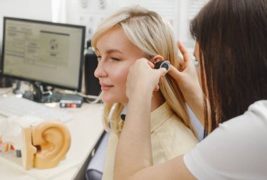 Kadın hasta doktor otolaringolojistte işitme kontrolü yapıyor. Kadın için işitme sınavı. Otolaryngologist doktor, tıbbi klinikte otoskop ya da auriskop kullanarak olgun kadınların kulaklarını kontrol ediyor.