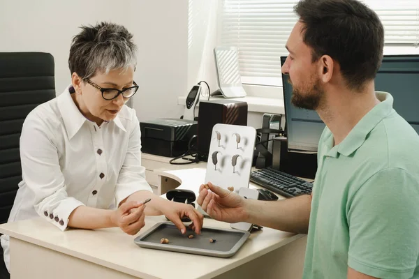 Adam klinikte modern kompakt işitme cihazı deniyor. İşitme rehabilitasyon kliniğinde orta yaşlı adam için dijital cihaz seçilmesi konusunda ses bilimci danışmanlık yapıyor. Doktor danışman hasta.
