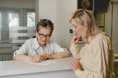 Kliniğin resepsiyonundaki hasta randevusundan bahsediyor. Kadın resepsiyonist, sağlık merkezindeki müşteriden başvuru formu alıyor. Dostça hizmet