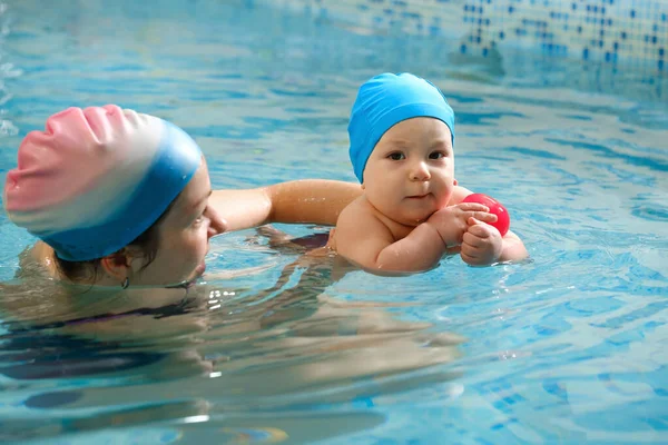 Havuzda erken yaşta yüzmek. Bebek suda yüzmek için eğitildi. Kapalı havuzda oynayan ve eğlenen antrenör kadından mutlu bir çocuk. Bebek, aktif ebeveyn ve sağlıklı ve spor ailesi