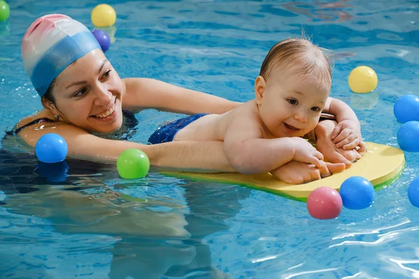 Havuzda erken yaşta yüzmek. Bebek suda yüzmek için eğitildi. Kapalı havuzda oynayan ve eğlenen antrenör kadından mutlu bir çocuk. Bebek, aktif ebeveyn ve sağlıklı ve spor ailesi