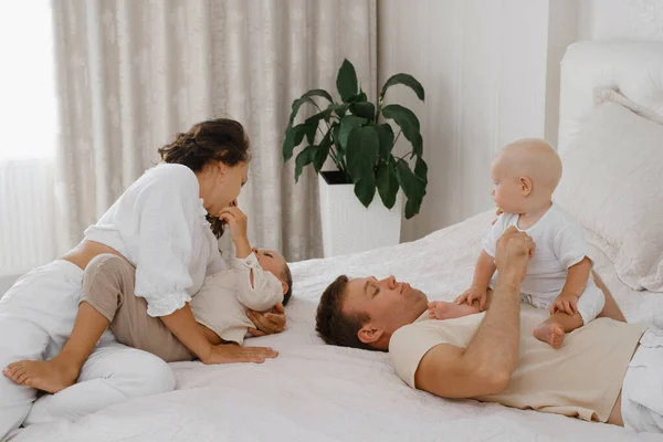 ベッドに2人の子供がいる家族が楽しんでいます 赤ちゃん 幼児の息子たちは 朝寝室で幸せに暮らしています 自宅で両親と遊んでいる子供たち 現実の生活と幸福 — ストック写真