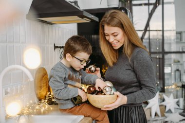 Anne ve çocuk Noel mutfağında dekor ve takılarla ödeme yapıyorlar. Kadın ve oğlu Noel kutlaması için evi hazırlıyorlar. Bokeh ve gerdanlar şenlik havası yaratıyor. Noel iç dekorasyonu