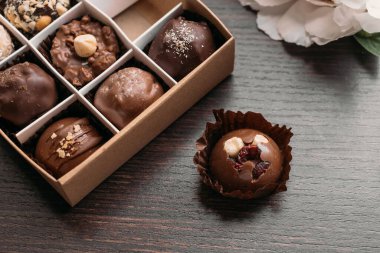 Karanlık masadaki kutuda el yapımı çikolatalı şekerler. Fındıklı çikolata, kurutulmuş meyve ve meyveler hediye kutusunda.