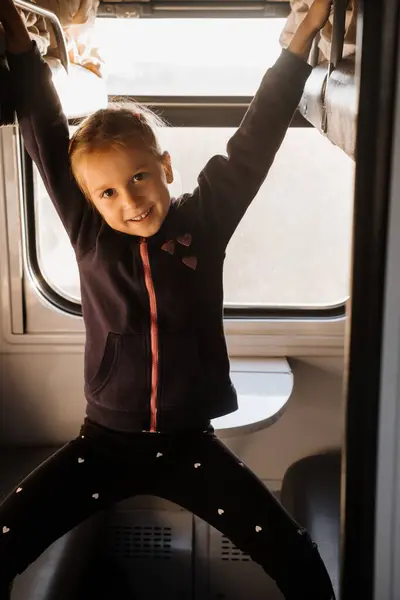 Happy child riding in train on sunset, bright sunlight, atmospheric travel by railway with kids. Young passenger playing on the couch of slipping wagon. Long family trip