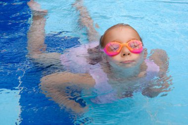 Yüzme havuzuna dalan çocuk. Bebek gözlüklerle suya atlıyor ve yüzmeyi öğreniyor. Kız suda eğleniyor, Aquapark 'ta baloncuk yapıyor