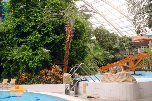 Aquapark 'ın içi. İçinde köprü ve yüzme havuzları olan yeşil palmiye ağaçlarıyla dolu kapalı macera parkında hidromasaj, kapalı küvetli dinlenme alanı.