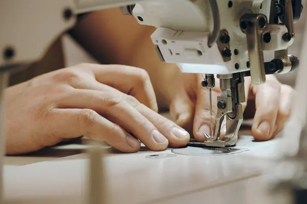 Tailor sewing at workplace. Man hands sewing on machine at his studio. Tailoring concept. Close-up of needle and thread in male hands