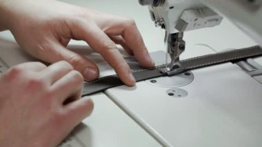 İş yerinde terzilik. Adam elleri atölyesinde makineye dikiş dikiyor. Terzilik konsepti. Erkek ellerindeki iğne ve ipliğe yakın çekim
