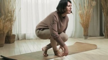 Yoga yapan bir kadın. 50 'li yaşlarda orta yaşlı bir kadın mindere oturmuş meditasyona ve zihin konsantrasyonuna hazır..