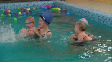 Çocuklar öğretmenleriyle kapalı havuzda yüzmeyi öğreniyorlar. Birlikte mutlu zaman geçirmek ve çocuklar için genel fiziksel aktivite, erken gelişim. Çocuk erken gelişiyor. Sıçra, zıpla