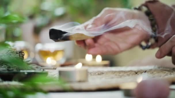 女人的手在点燃圣帕罗之前 先用蜡烛和绿色的植物在桌上做礼拜 烟熏治疗疼痛和压力 清除负面能量 冥想木棍 — 图库视频影像