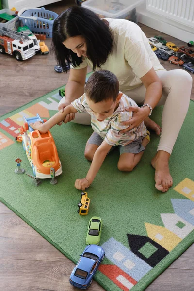 Kid with health problem playing toy cars with mother at home. child having Cerebral palsy entertaining on mat with caregiver Inclusion, rehabilitation in family for people with special needs