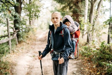 Man hiking with sleepy toddler child in the mountain. Kid sitting in backpack on father back. Active family adventure in forest with tired girl. Cold weather trip, Nordic walk tour clipart
