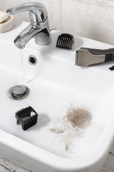 Cleaning electronic shaving razor in sink, male self care and personal hygiene Top view. Hair in sink. Long blonde hair, machine