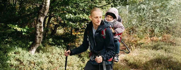 Banner Sleepy tired child walking with father in backpack in the mountains. Nordic walk with family and kid in fall. obstacles and challenges for man traveling outdoors. Adventure hiking tour