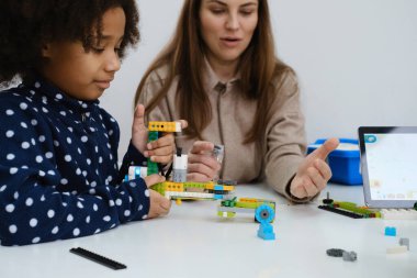 STEM dersindeki çoklu etnik çocuklar, kadın öğretmenle sınıfta robot inşa ediyorlar. Çocuklar, modern bilim okulunda Afrika kökenli Amerikalı, Kafkas öğrencilerin öğrenme teknolojisinde elektronik kol modeli yapıyorlar.