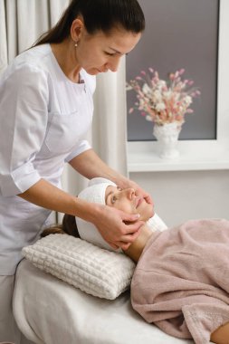 Müşteri kadın dermatoloji kozmetik uzmanıyla masaj yaptırıyor klinikte, cilt sorunlarıyla ilgili. Tedavi için bölgeleri gösteren bir kadın. Kuaförde prosedürden önce müşteriyle güzellik uzmanı