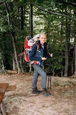 Man hiking with sleepy toddler child in the mountain. Kid sitting in backpack on father back. Active family adventure in forest with tired girl. Cold weather trip, Nordic walk tour clipart