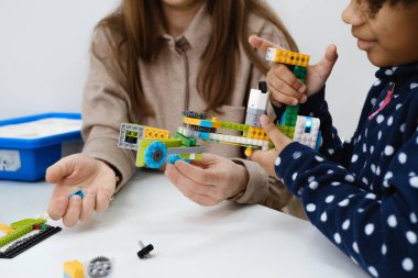 STEM dersindeki çoklu etnik çocuklar, kadın öğretmenle sınıfta robot inşa ediyorlar. Çocuklar, modern bilim okulunda Afrika kökenli Amerikalı, Kafkas öğrencilerin öğrenme teknolojisinde elektronik kol modeli yapıyorlar.