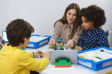 STEM dersindeki çoklu etnik çocuklar, kadın öğretmenle sınıfta robot inşa ediyorlar. Çocuklar, modern bilim okulunda Afrika kökenli Amerikalı, Kafkas öğrencilerin öğrenme teknolojisinde elektronik kol modeli yapıyorlar.