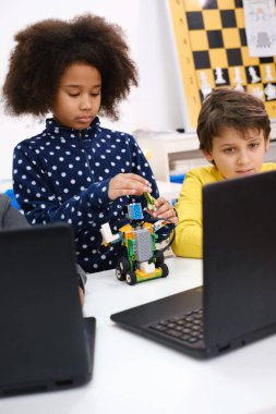 Çocuklar okulda kodlama, fen ve teknoloji öğreniyor. Afrika kökenli Amerikalı ve Kafkasyalı çocuklar STEM dersinde dizüstü bilgisayarlarıyla geziyorlar. Modern yenilikçi eğitimde çeşitlilik