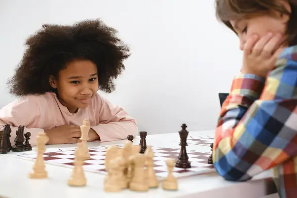 Diverse Group of kids playing chess. Concentrated multiethnic clever children with board game having fun at school. African American girl and Caucasian boys on chess lesson strategy