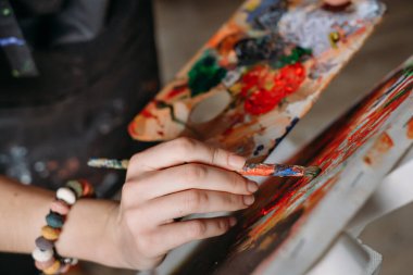 Gerçek stüdyoda yağlı boyalarla çalışan, tuval yapan, modern sanat eserleriyle uğraşan bir ressam. Genç kadın ressam, paletin üst görüntüsü.