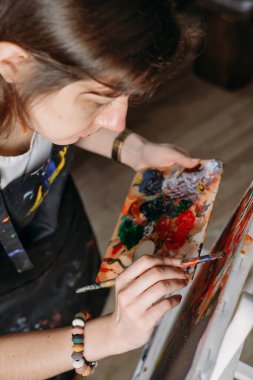 Yağlı boya boya ve fırçalarla gerçek bir stüdyoda çalışan ressam tuval ve modern sanat eserleri yaratıyor. Pencerenin oradaki genç bayan, yakın plan.