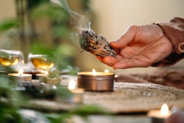 Masada mumlar ve yeşil bitkilerle ayin yapılmadan önce kadın elleri beyaz adaçayı yakıyordu. Leke dumanı acı ve stresi tedavi eder, temiz negatif enerji ve meditasyon.
