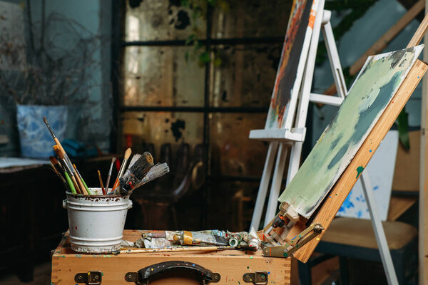 Творческий фон на холсте, работа в настоящей студии с масляными красками и кисточками, картина современного искусства. над окном, при свечах. Рабочее пространство художника