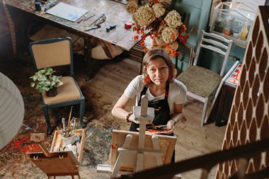 Yağlı boya boya ve fırçalarla gerçek bir stüdyoda çalışan ressam tuval ve modern sanat eserleri yaratıyor. Paletli genç adam, yakın plan.