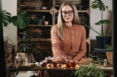 Kadınlar boho tarzı atmosferik odada çay seremonisi hazırlıyorlar. Stüdyoda bitkiler var. Ellerinde sıcak içecek olan şeffaf çay fincanları. Geleneksel Oolong Çin içkisi.