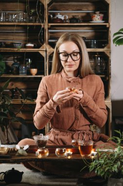 Kadınlar boho tarzı atmosferik odada çay seremonisi hazırlıyorlar. Stüdyoda bitkiler var. Ellerinde sıcak içecek olan şeffaf çay fincanları. Geleneksel Oolong Çin içkisi.