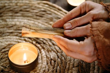Kadın elleri Palo Santo 'yu yakmadan önce, masada mumlar ve yeşil bitkilerle. Leke dumanı acıyı ve stresi tedavi eder. Negatif enerjiyi ve meditasyon çubuğunu temizler.