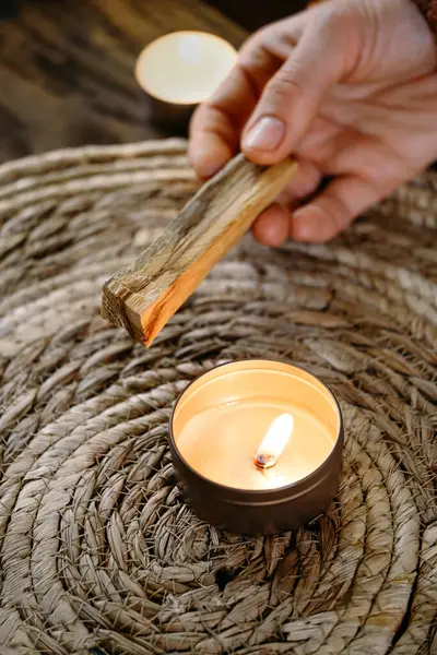 Kadın elleri Palo Santo 'yu yakmadan önce, masada mumlar ve yeşil bitkilerle. Leke dumanı acıyı ve stresi tedavi eder. Negatif enerjiyi ve meditasyon çubuğunu temizler.
