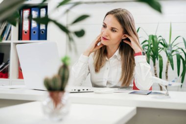 İletişim için dizüstü bilgisayar ve akıllı telefon kullanan rahat iş kadını ve bitkilerle modern çevrede çalışıyor. Seyahat acentesi zor zamanlar