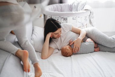 Evde iki çocuğu olan bir anne emziriyor. Bebek annesinin ellerinden emzirirken ablası da yanında zıplama oyunu oynarken küçük kızıyla konuşurken bir bebeğe sarılıyor.