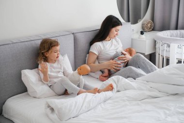 Emziren anne evde. Bebek anne ellerinden emziriyor, bir bebeğe sarılıyor ve oğluyla konuşuyor.