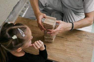 Çocuk ve yetişkin, kapalı bir masada birlikte ahşap kule oyunu yapmaya odaklanmış. Baba ve kızı boş zamanın tadını çıkarıyorlar. Kaliteli aile ilişkileri ve gayri resmi eğitim