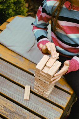 Tahta blokları istiflemek, açık bir masada otururken kule inşa etmek, parçaları dengelemeye konsantre olmak. Yakın çekim.