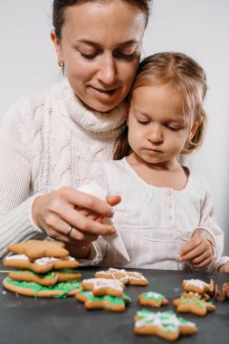 Anne ve çocuk Noel için zencefilli kurabiyeleri kremayla süslüyor. Ev yapımı şenlik yemekleri. Şirin küçük kız Aile Atölyesi. Yıldızlar, ağaç